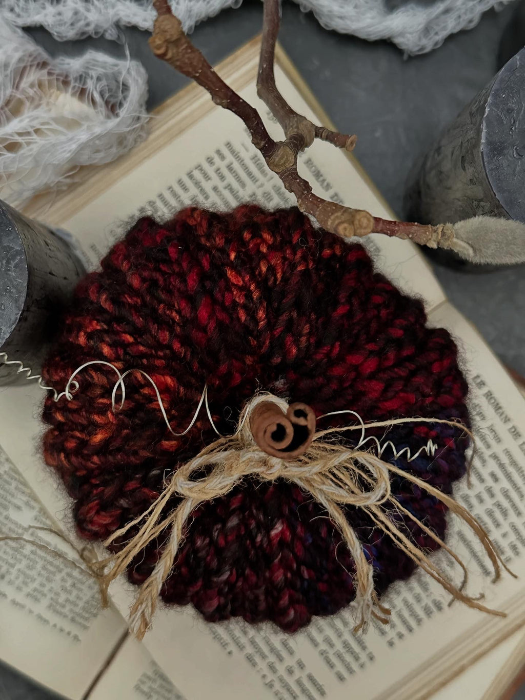 A crocheted pumpkin featured from above made from black and jewel tone variegated yarn, with twine bow and cinnamon stick stem, styled on open vintage books and surrounded by rustic props.