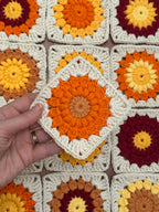 Hand holding a crochet granny square with sunflower pattern above a background of more crocheted granny squares.