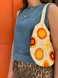 Woman wearing a denim shirt and leopard shorts with a colourful crochet bag over their shoulder against an orange door.