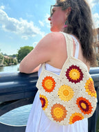 Woman holding a colourful crochet bag by a river